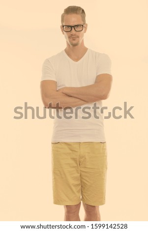 Young handsome man standing while wearing eyeglasses with arms crossed