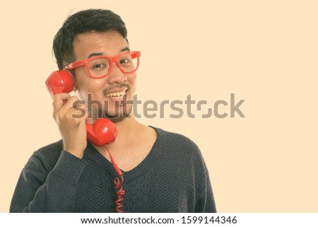 Close up of young happy Asian man smiling while talking on old telephone