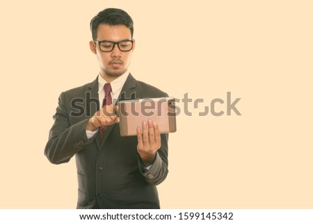 Studio shot of young Asian businessman using digital tablet