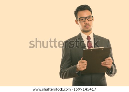 Studio shot of young Asian businessman holding clipboard