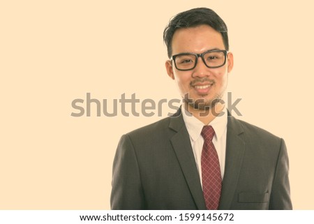 Studio shot of young happy Asian businessman smiling while wearing eyeglasses