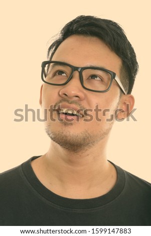 Face of young happy Asian man smiling and thinking while looking up