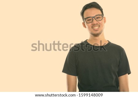 Studio shot of young happy Asian man smiling while wearing eyeglasses