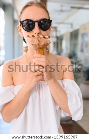 Outdoor closeup fashion portrait of young hipster crazy girl eating ice cream in summer hot weather in round mirror sunglasses have fun and good mood