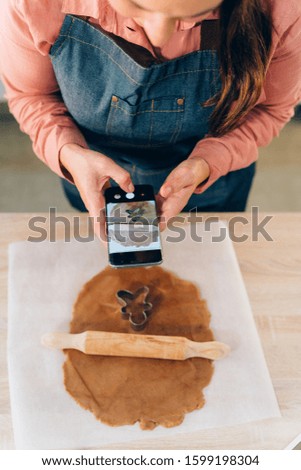 Young brunette woman making a photo of gingerbread man at home. Handmade gingerbread cookies for the Christmas Holidays.
