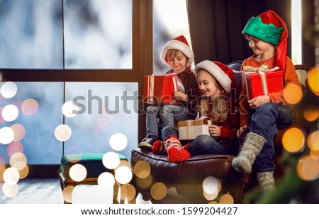Little children with Christmas gifts near window indoors. Presents from Santa Claus
