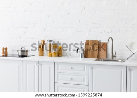 minimalistic modern white kitchen interior with kitchenware near brick wall