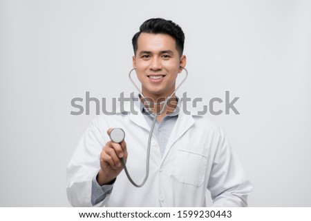 Portrait of a friendly handsome male doctor dressed in uniform holding stethoscope and looking at camera isolated over white background