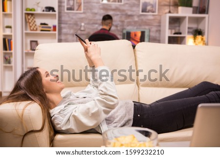 Beautiful young woman resting on sofa and browsing on sofa. Boyfriend in the background.