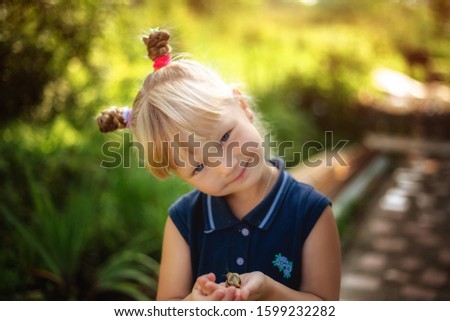 Little blonde girl holding a snail outdoors