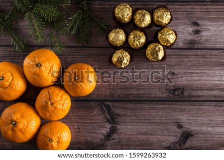 Chocolate candies in gold foil with tangerines on a wooden background with fir branches. Candy is an excellent and delicious gift for the New Year holidays and Christmas. The atmosphere of the holiday