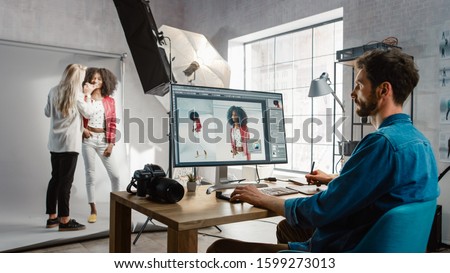 Backstage of the Photoshoot: Make-up Artist Applies Makeup on Beautiful Black Girl. Photo Editor Works on Desktop Computer Retouching Photo with Image Editing Software. Fashion Magazine Royalty-Free Stock Photo #1599273013