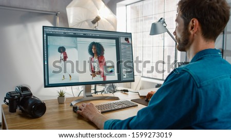 Professional Photographer Sitting at His Desk Uses Desktop Computer in a Photo Studio Retouches. After Photoshoot He Retouches Photographs of Beautiful Black Female Model in an Image Editing Software Royalty-Free Stock Photo #1599273019