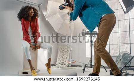Beautiful Black Model Posing for a Photographer, he Takes Pictures with Professional Camera. She plays with Facial Expressions. Stylish Fashion Magazine Photo Shoot done with Pro Equipment in a Studio