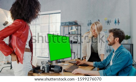 In Photo Studio Fashion Magazine Designer and Beautiful Black Cover Girl talk to a Professional Photographer who Uses Desktop Computer with Green Mock-up Screen Display