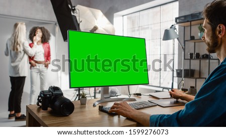 Backstage of the Photoshoot: Make-up Artist Applies Makeup on Beautiful Black Girl. Photo Editor Works on Desktop Computer with Green Mock-up Screen Display. Fashion Internet Magazine