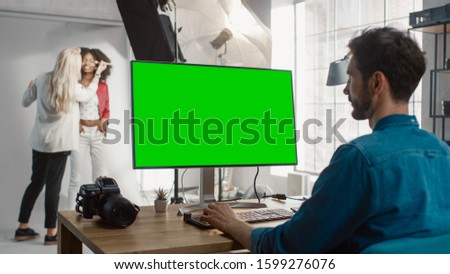 Backstage of the Photoshoot: Make-up Artist Applies Makeup on Beautiful Black Girl. Photo Editor Works on Desktop Computer with Green Mock-up Screen Display. Fashion Internet Magazine