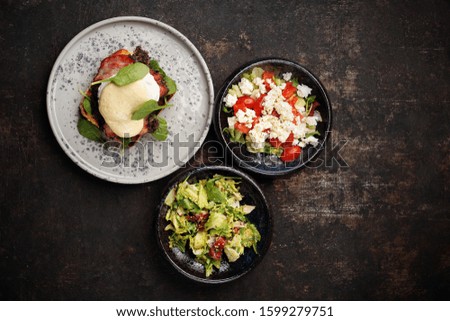Toast with black pudding, poached egg, bacon and mayonnaise sauce served with a patch of fresh green vegetables. Food, ready dish on a dark background. Suggestion of serving the dish. top view