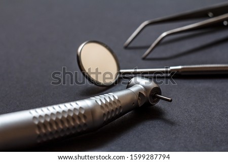 Set of metal dental instruments for dental treatment. High-speed dental handpiece, dental mirror and tweezers on black background. Medical tools. Shallow depth of field. Focus on the bur. Royalty-Free Stock Photo #1599287794