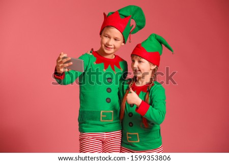 Little children in costume of elf taking selfie on color background