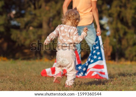 A little kid and a woman with a flag of United States of America in the hand, outdoors, soft focus background