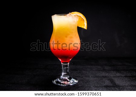 Tequila sunrise cocktail with ice and a slice of citrus. a glass with an alcoholic drink on a black, isolated background.