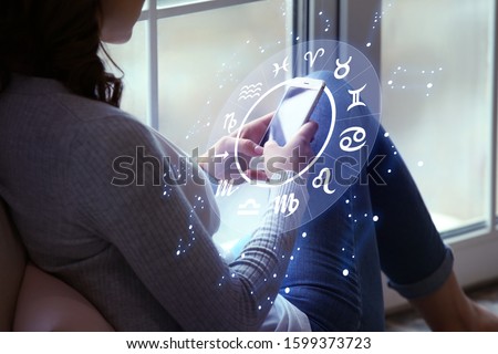 Young woman with mobile phone reading astrological forecast at home