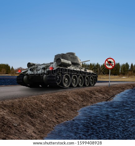 A funny image of a tank having stopped on the coast road before the "no tanks" traffic sign with stop lights on. Copy space on the upper and lower part of the photo.