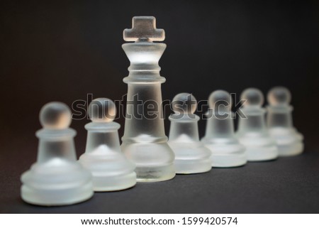 Glass chess pieces. King in front of pawns. Conceptual chess photo on a black background.