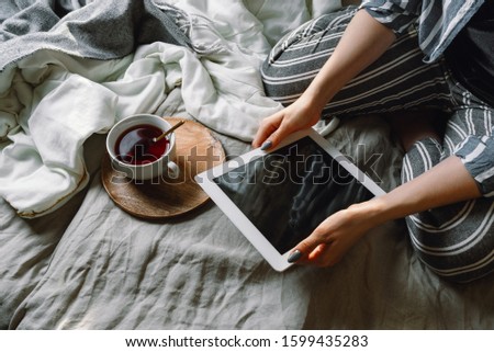 Faceless portait of woman holding a tablet in her bed with cup of tea, selective focus