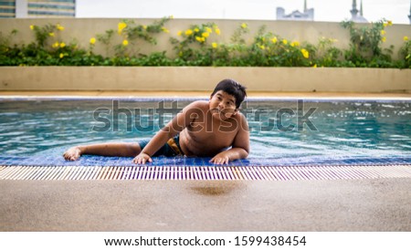 Young asian happy kid swimming inside the swimming pool at the resort during the summer. Joy face expression. Holidays activity.
