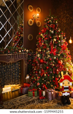 Christmas decor. Expensive beautiful red Christmas decorations, fireplace, Christmas tree, Nutcracker, mirror, gifts in the dark living room in a country Chalet.