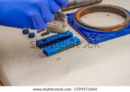 Worker paints a metal vise with blue paint. Stripping old paint.