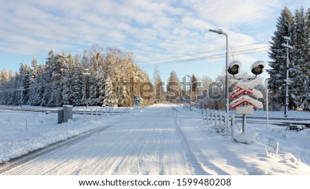 A sunny, snowy winter day. Rail and highway junction without barrier. Warning signs at the rail level crossing. Traffic safety.