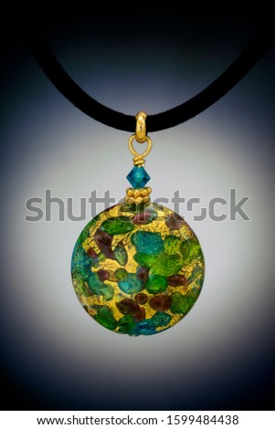 A handcrafted multi-colored glass lollipop shape bead is featured in this pendant with gold findings. Shown on a velvet cord and against a vignetted background.