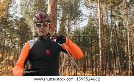 Training an athlete on the roller skaters. Biathlon ride on the roller skis with ski poles, in the helmet. Autumn workout. Roller sport. Adult man riding on skates. Athlete is getting ready to start.