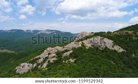 Aerial view of hilly region with mountains on the background of blue sky with clouds. Shot. Flying over the mountains covered dense green forest and rock formations.