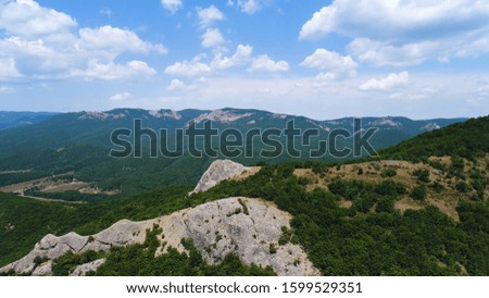 Aerial view of mountain rocks with a vast valley on blue cloudy sky background. Shot. Natural breathtaking landscape with green trees, rocks, and hills.