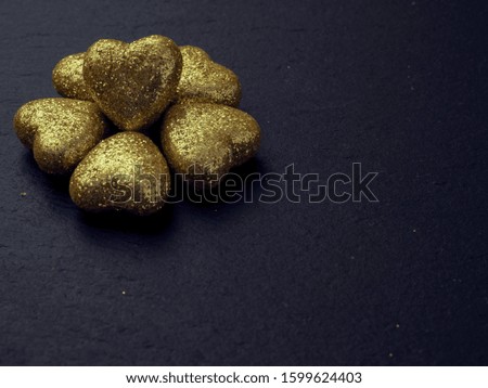 Golden hearts with glitter on a dark surface, Saint Valentine theme background.