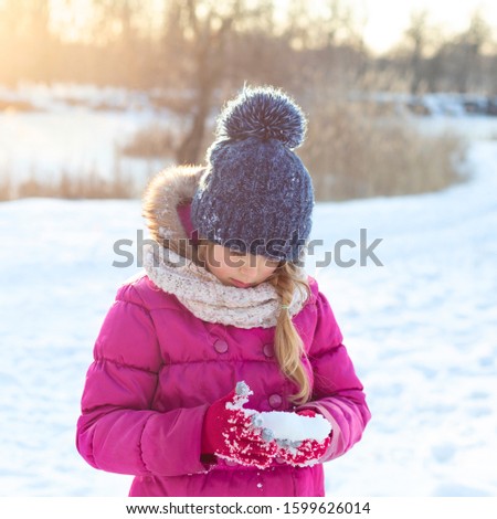 Pretty little girl wearing pink jacket and knitted hat walking in snowy winter park. Child playing with snow in forest. Family vacation with child in mountains	