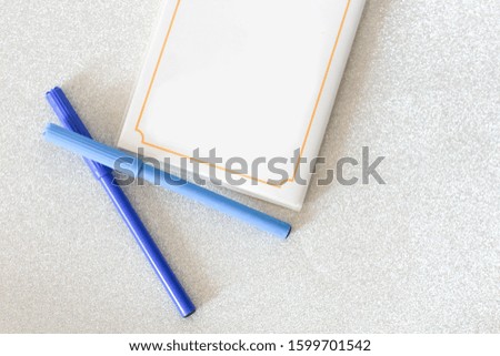 White notebook with blue pen on sparkling silver background. Selective focus
