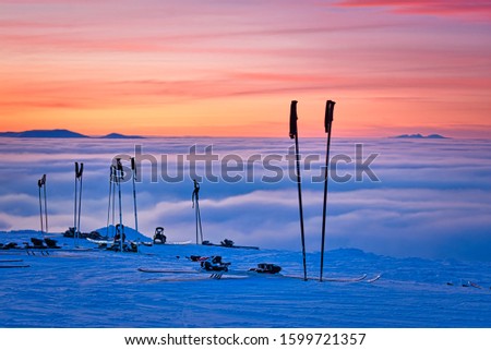 Ski poles and skis resting at the top of a mountain in Sweden during the winter. Low clouds and a fabulous orange and pink sunset add to the drama, enhanced with a very shallow depth of field.