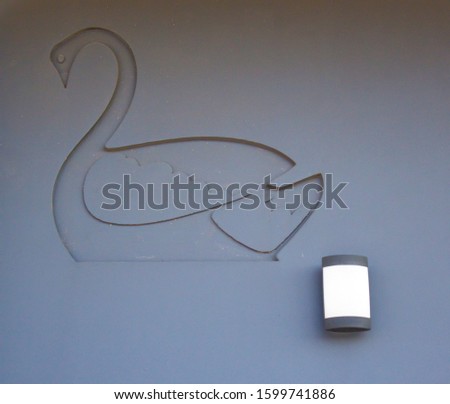 An outline of a black swan has been etched into a plain grey concrete wall with a white light adding a pretty pattern .