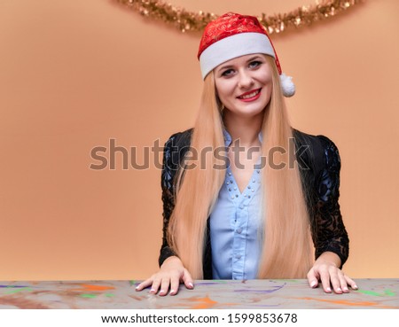 Portrait of a woman in a business suit with long beautiful hair and excellent make-up with New Year's decor on a pink background. The concept of the New Year mood of a blonde girl sits at a table.