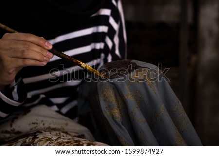 close photo of a woman working on a West Java batik motif with a brush