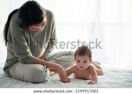 Mother and child on a white bed. Mom and baby boy in diaper playing in sunny bedroom. Parent and little kid relaxing at home. Family having fun together. Bedding and textile for infant nursery