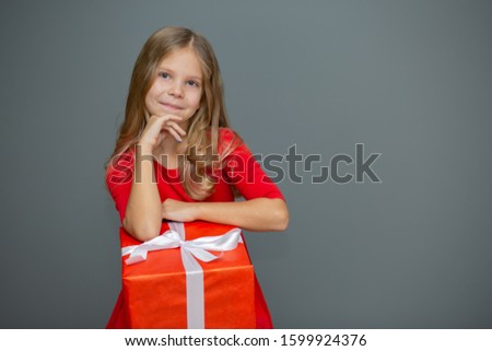 
beautiful blonde girl in a red dress with a gift and happy emotions on a gray background, a gift for the new year, March 8, Valentine's Day, mother's day