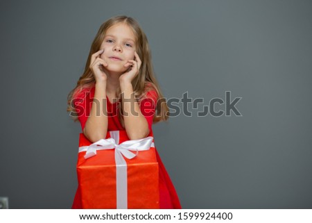 
beautiful blonde girl in a red dress with a gift and happy emotions on a gray background, a gift for the new year, March 8, Valentine's Day, mother's day