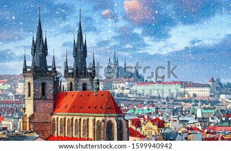 High spires towers of Tyn church in Prague city (Church of Our Lady before Tyn cathedral) urban landscape panorama with red roofs of houses in old town and blue sky with snowfall and clouds.