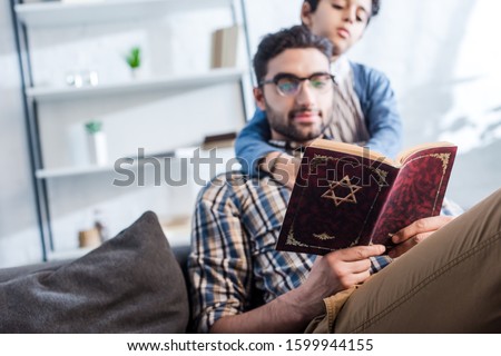 selective focus of jewish father and son reading tanakh in apartment  Royalty-Free Stock Photo #1599944155